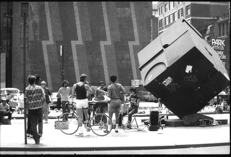 Alamo Sculpture, mural, vendors, & musicians on Astor Place, looking south from 8th Street, between Lafayette Street and Cooper Square. 1980s.<br/>